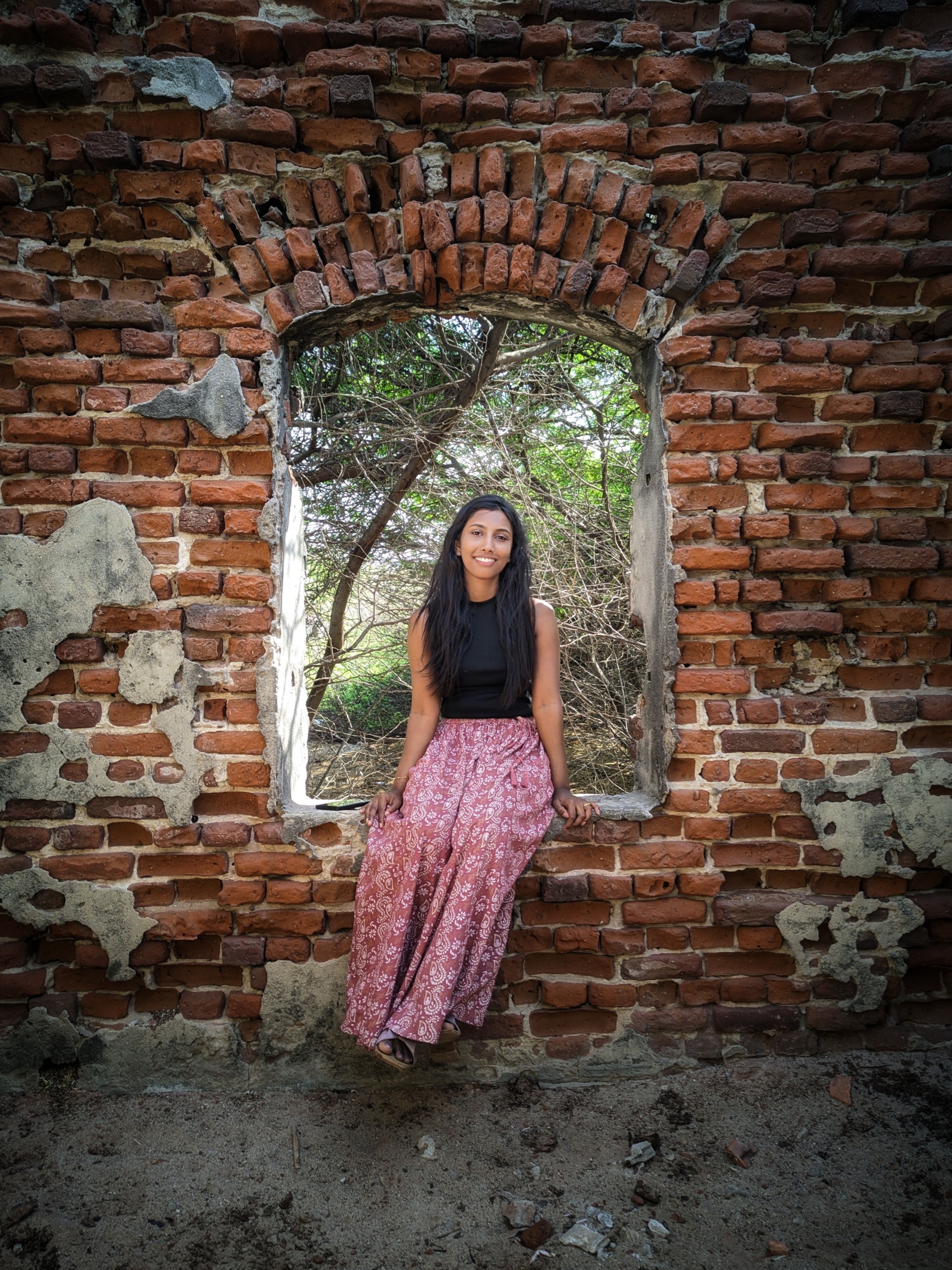 A woman poses in a rustic brick window at the historic site in Dhanushkodi, India.