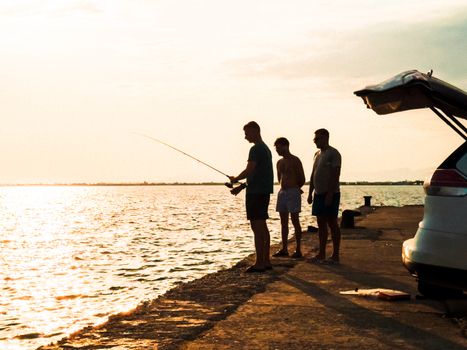 Three men fishing off a pier during sunset, enjoying a peaceful moment by the water.