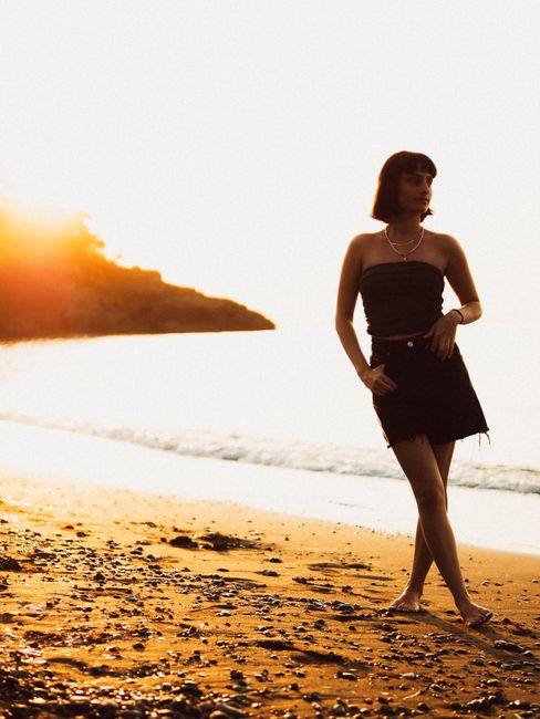 Woman in summer attire walking on sunset beach with glowing backdrop.