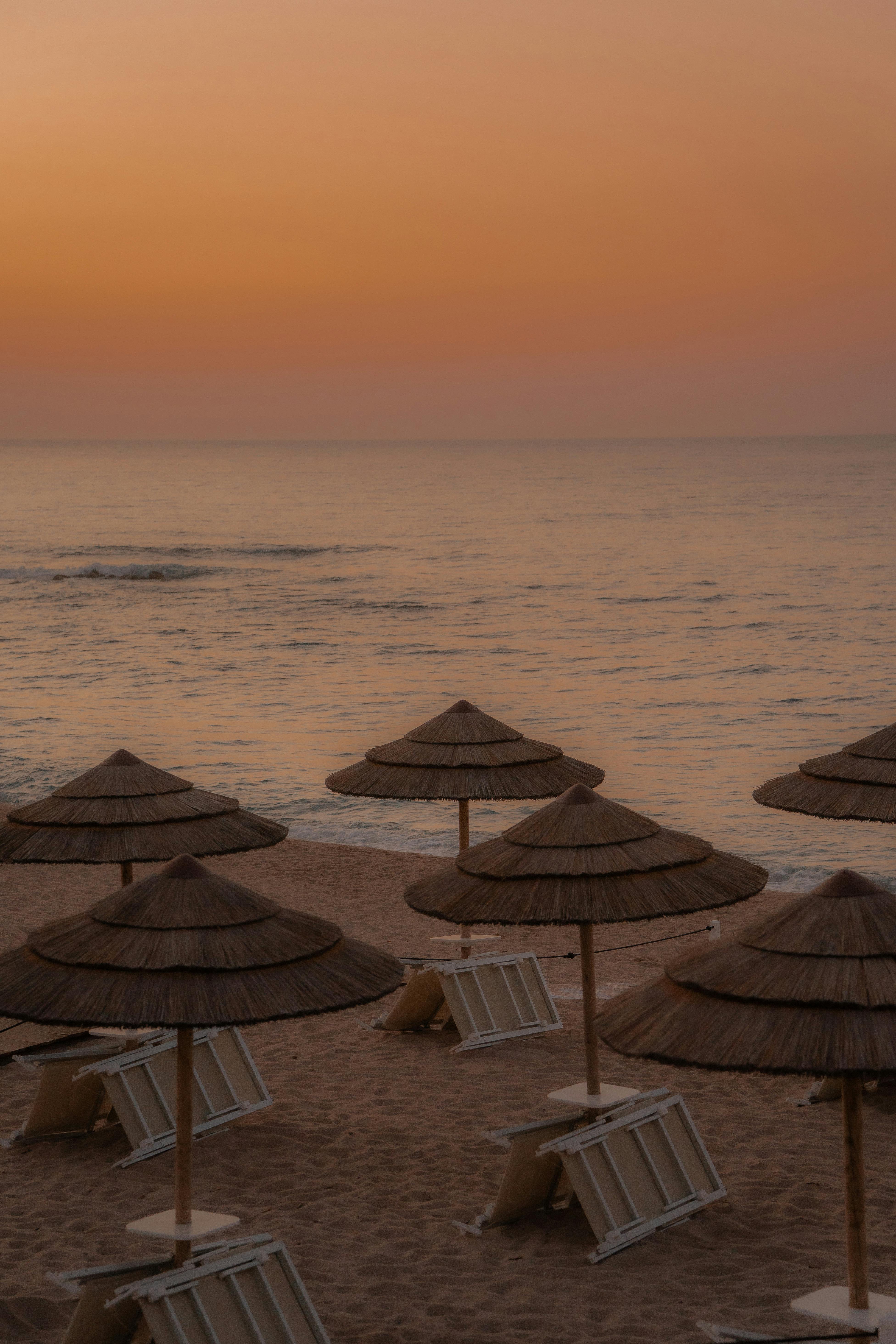 A peaceful beach scene at sunset with straw umbrellas and calm seas.