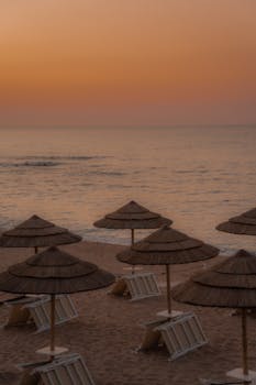 A peaceful beach scene at sunset with straw umbrellas and calm seas.
