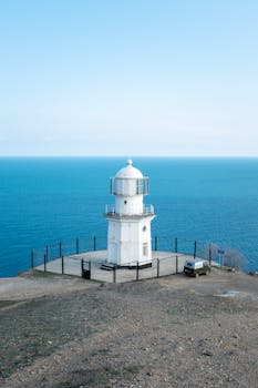 A white lighthouse stands on a cliff overlooking the blue sea in Russia, offering stunning coastal views.