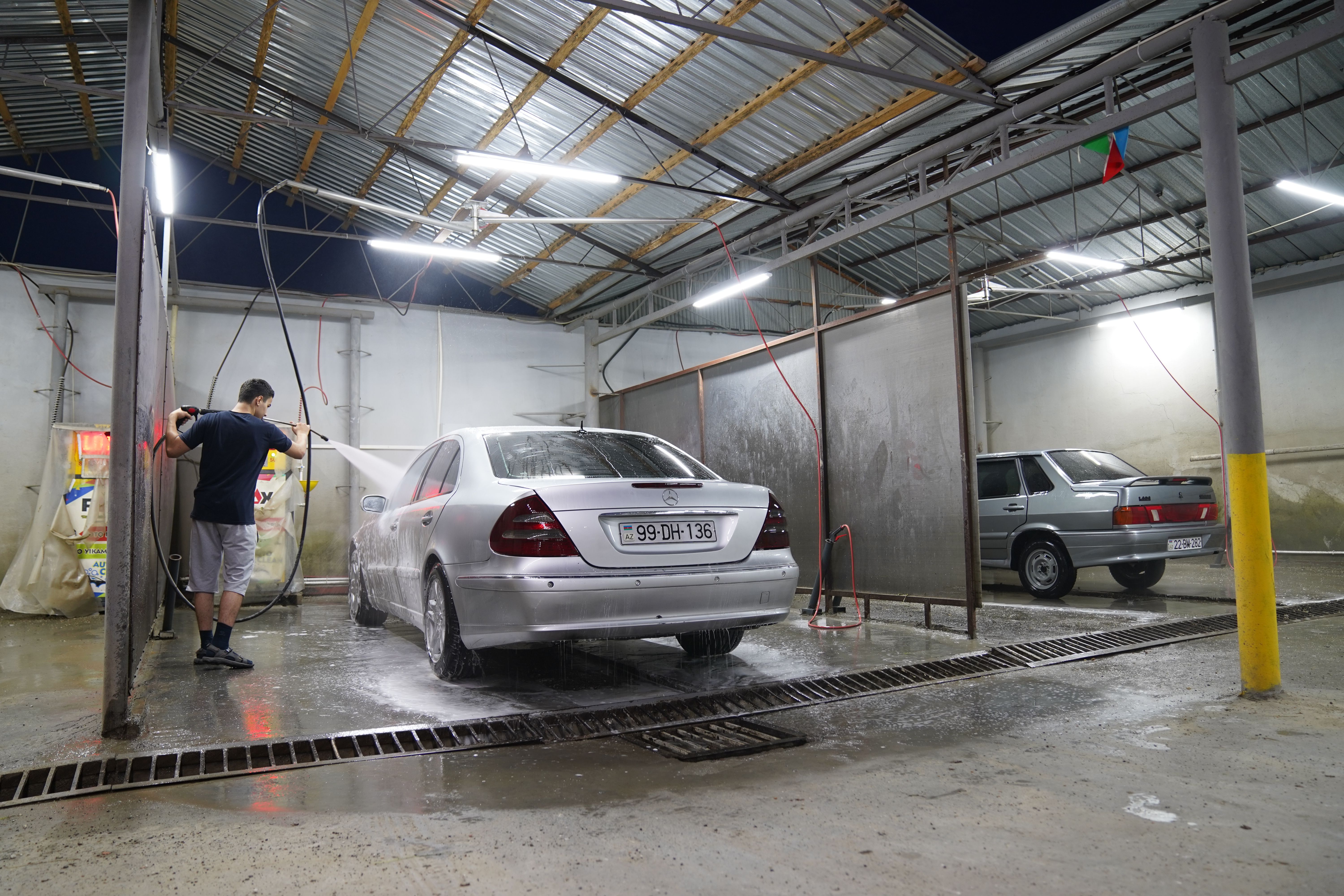 Homem lavando um carro prateado com jato de água em garagem coberta à noite