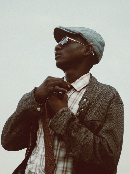 Free Man in a cap adjusting his tie, wearing sunglasses and a jacket outdoors. Stock Photo