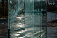 A broken glass bus stop with reflections, suggesting urban decay and vandalism.