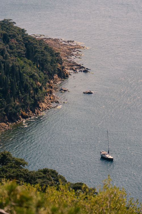 Free A serene coast with a sailboat, lush greenery, and clear blue water on a summer day. Stock Photo