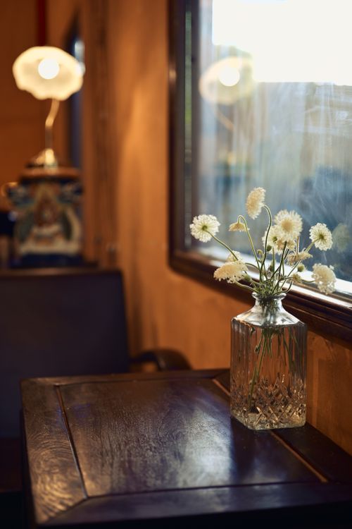 Free A cozy café setting with a glass vase holding delicate white flowers on a wooden table. Stock Photo
