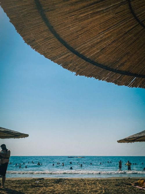 Free Serene beach scene with sunbathers enjoying a sunny day under straw umbrellas. Stock Photo