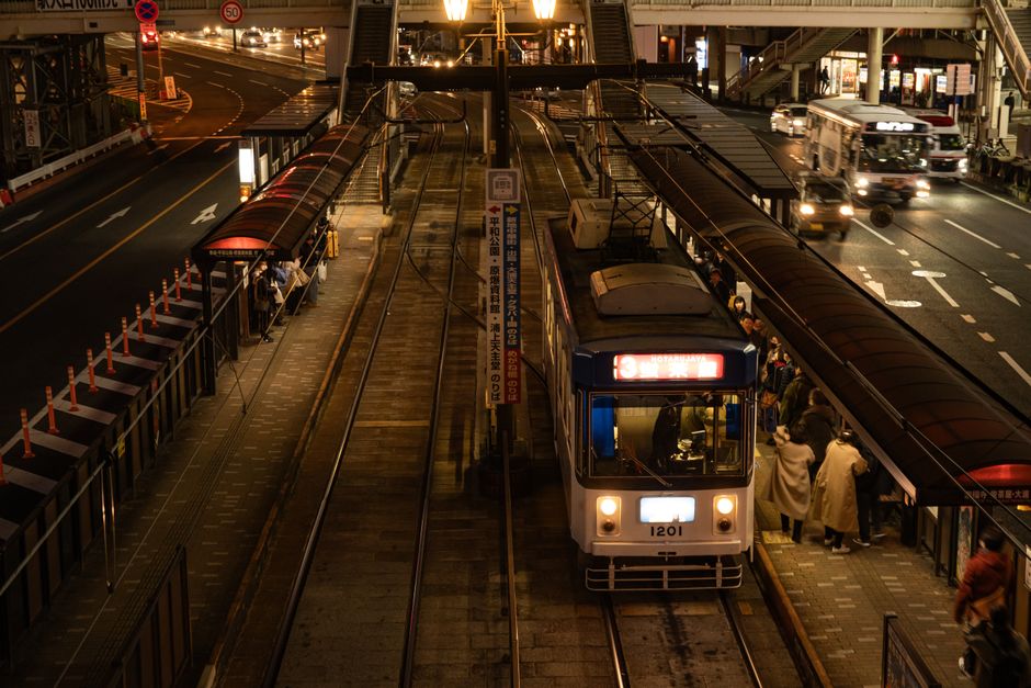 View of a bustling tram station in Nagasaki at night, people boarding.