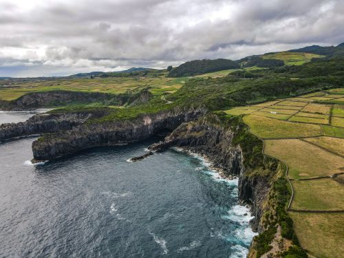 Free Aerial view of stunning coastal cliffs and lush green fields under cloudy skies. Stock Photo