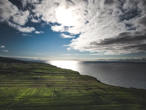 A stunning aerial view of a coastal landscape with lush green fields meeting the expansive ocean under a dramatic sky.