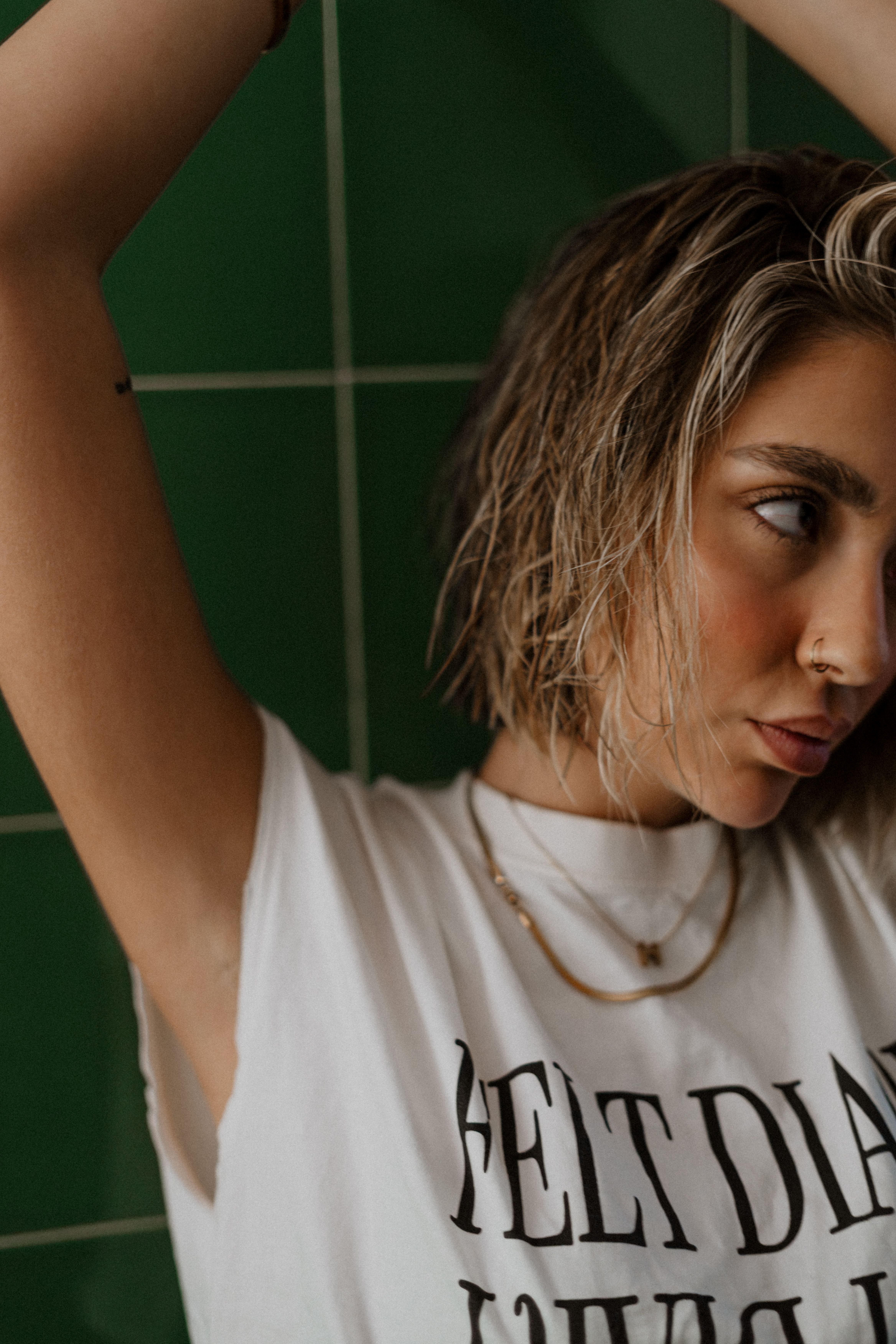 Stylish woman with short hair poses in white shirt against green tiles. Fashion and attitude.
