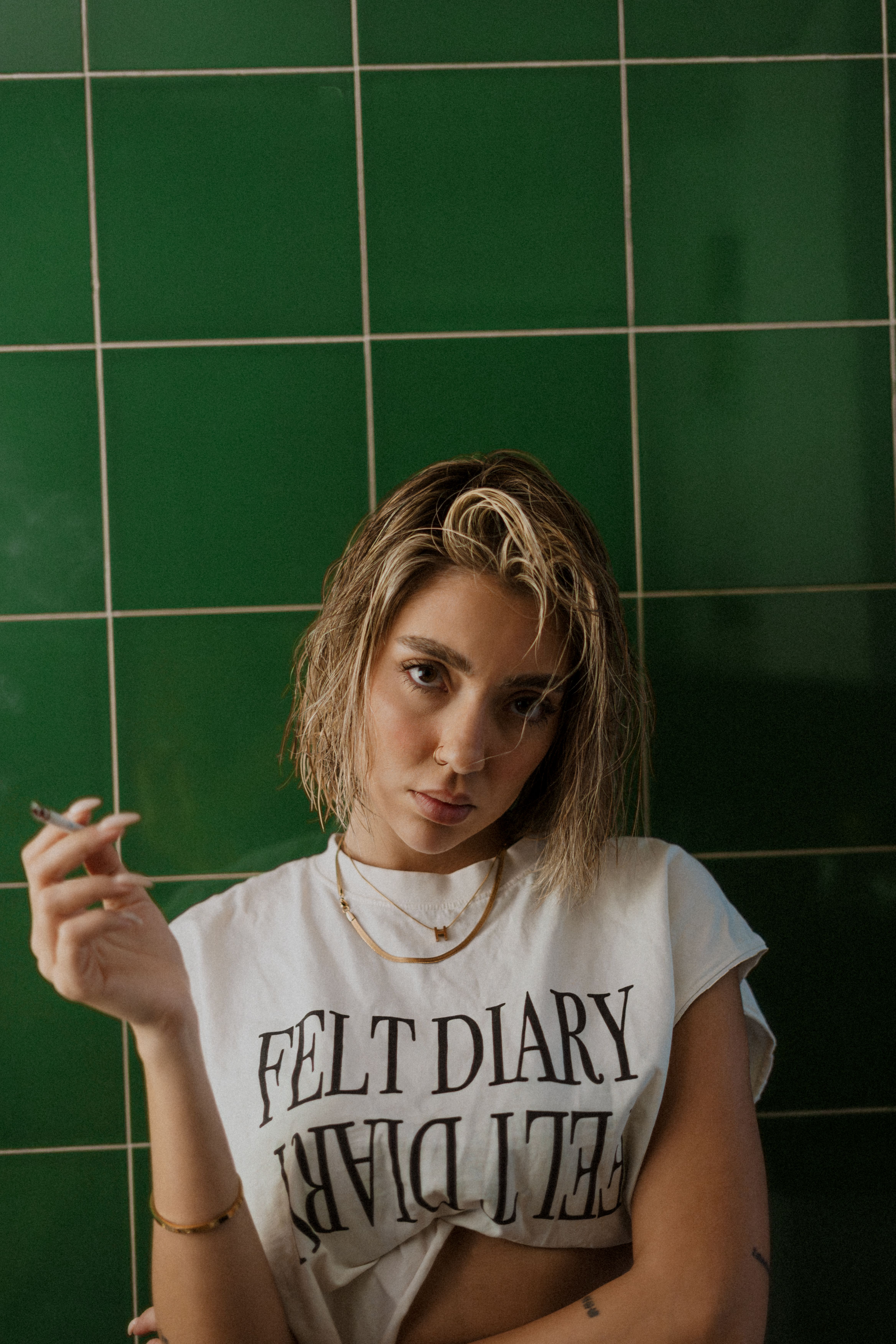 Fashionable woman poses with cigarette against green tiles, exuding cool confidence.