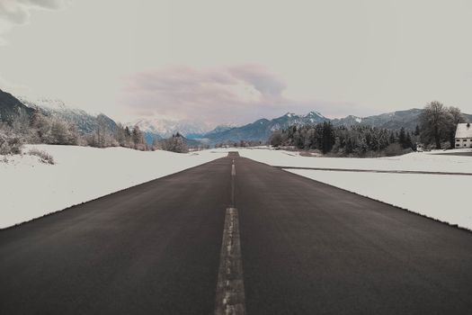 冬日里，一条道路在多云的天空下延伸，通向白雪皑皑的山脉
