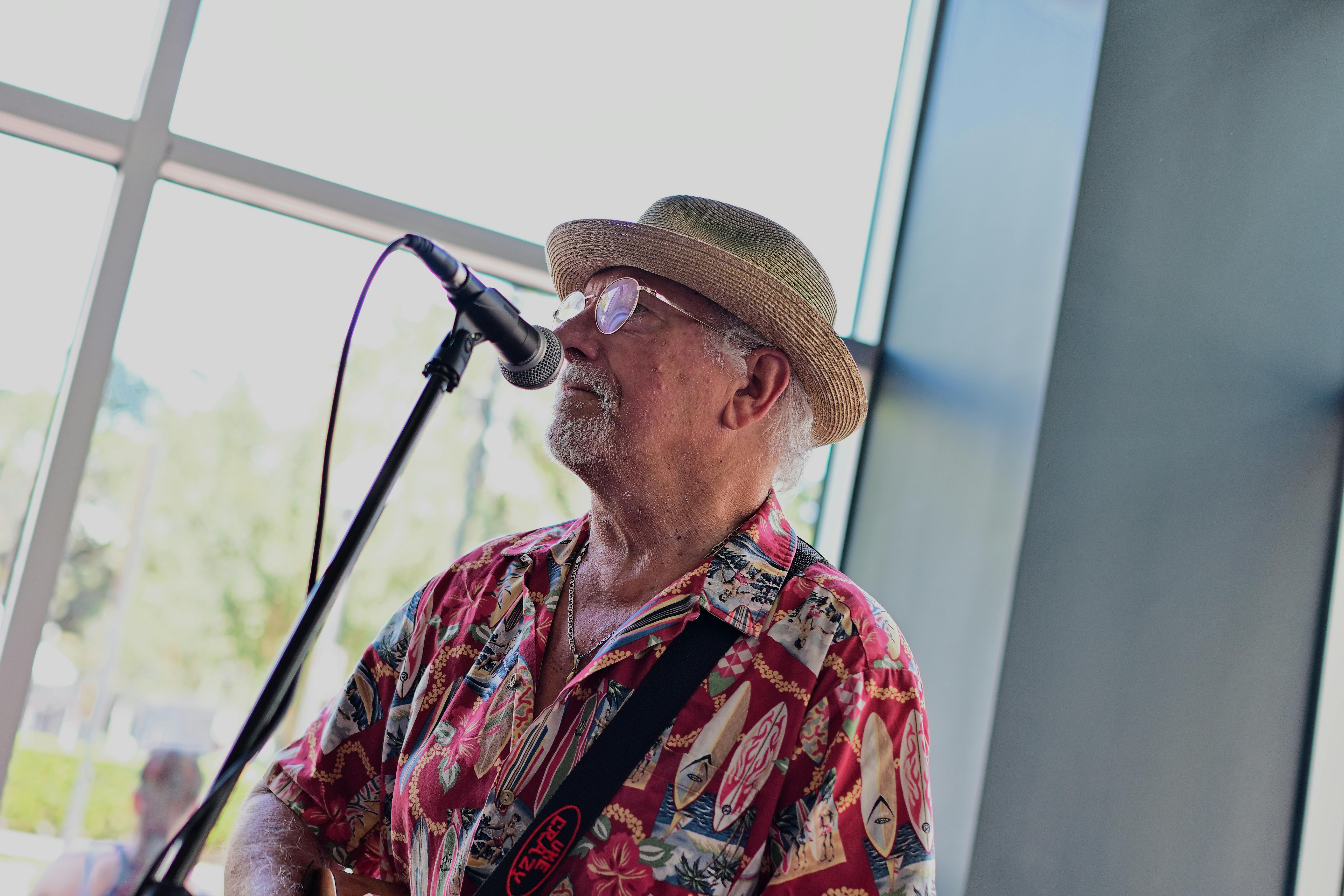 Senior male musician singing with microphone indoors, wearing Hawaiian shirt.