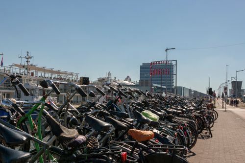 Free A row of parked bicycles by the waterfront in Amsterdam with modern buildings and boats in the background. Stock Photo