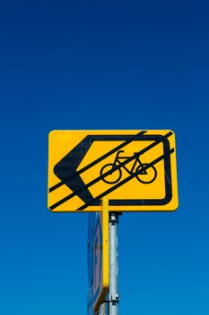 Yellow bicycle lane traffic sign with arrow on a clear blue sky background, highlighting transportation safety.