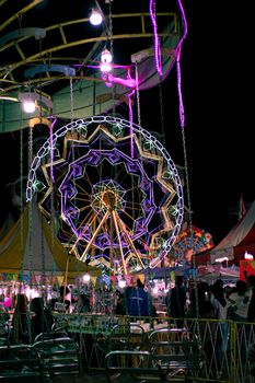 Colorful Ferris wheel lights up the night at Bali's lively carnival, creating a festive atmosphere.