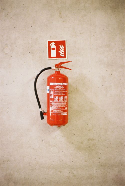 Free A red fire extinguisher mounted on a concrete wall with safety signage. Stock Photo