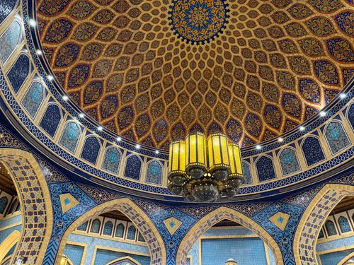 Free A stunning Islamic dome with intricate blue and gold geometric patterns and central chandelier. Stock Photo