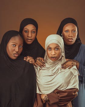 Four women in hijabs with intricate henna designs pose against a warm backdrop.