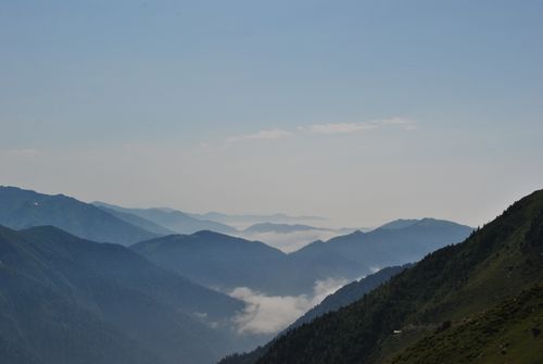 Free Stunning mountain landscape with rolling hills and misty clouds under a sunny sky. Stock Photo