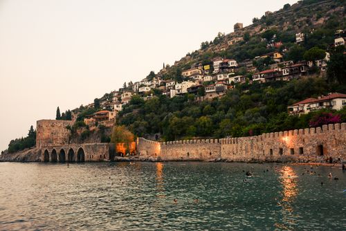 Free Historic seaside fortress with hilltop houses at dusk, featuring calm waters and warm lighting. Stock Photo