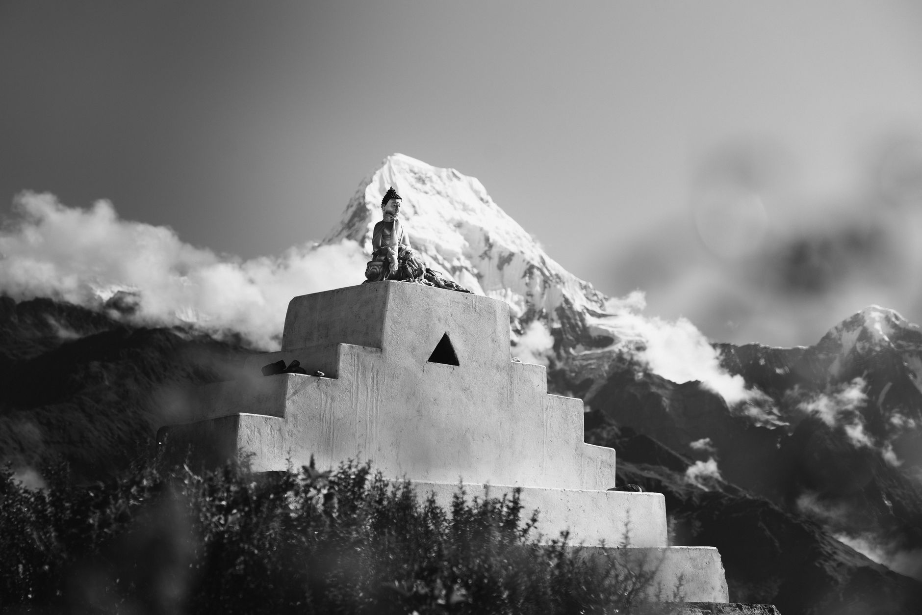 Black and white image of a Buddha statue with Annapurna backdrop, serene and majestic.