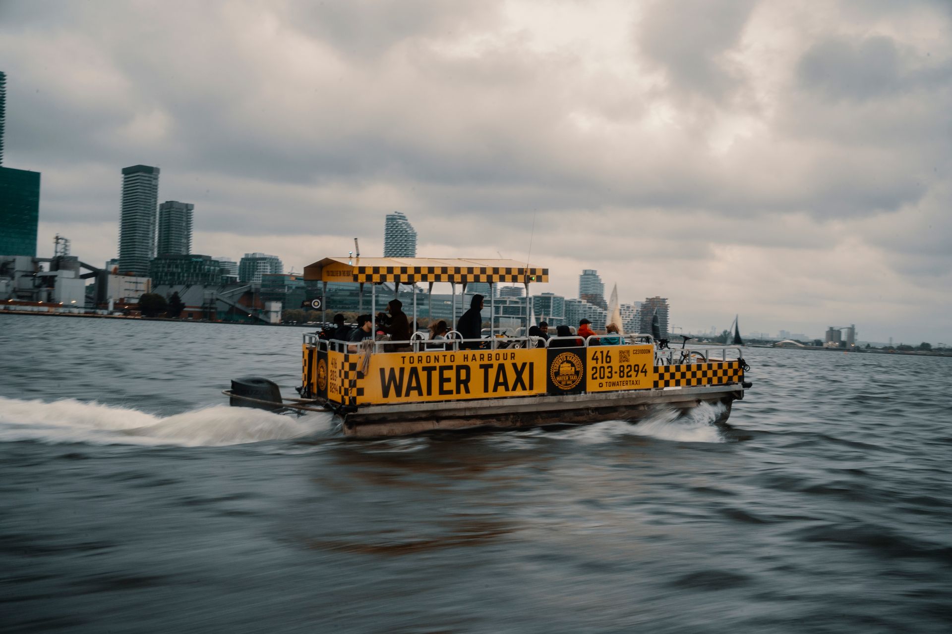 Water taxi navigating Toronto Harbour with city skyline in the background on a cloudy day.