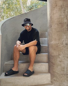 Man in bucket hat and sunglasses sitting on modern concrete staircase in Mexico.