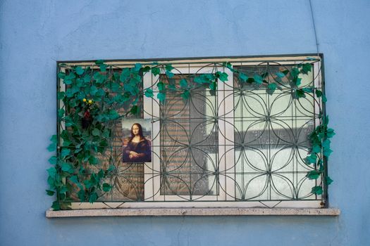 Window with decorative grill, green ivy, and Mona Lisa poster on a blue wall.