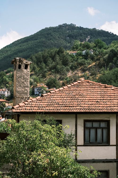 Free Charming rustic house with red tile roof against a scenic green mountain backdrop. Stock Photo