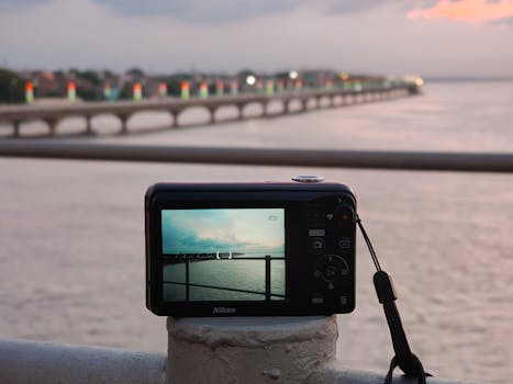 A Nikon camera capturing a serene view of a bridge at sunset over a calm river.