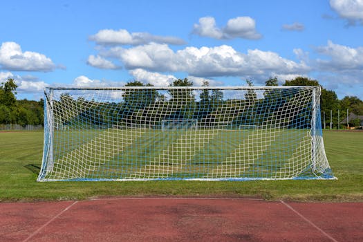 A soccer goalpost on an empty field beneath a blue sky with clouds, capturing a typical sporting scene.