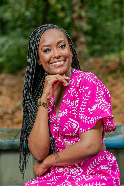 Free A cheerful woman with braids in a vibrant pink dress seated outdoors in Bahia, Brazil. Stock Photo
