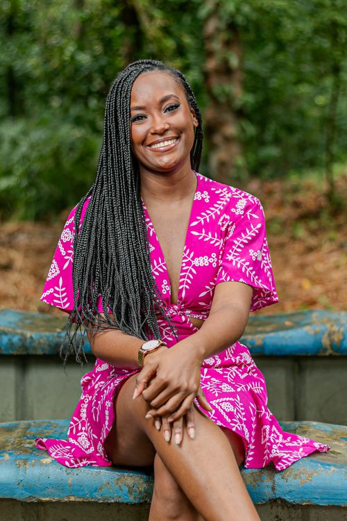 Free A cheerful woman with braided hair sitting outside wearing a bright pink dress. Stock Photo