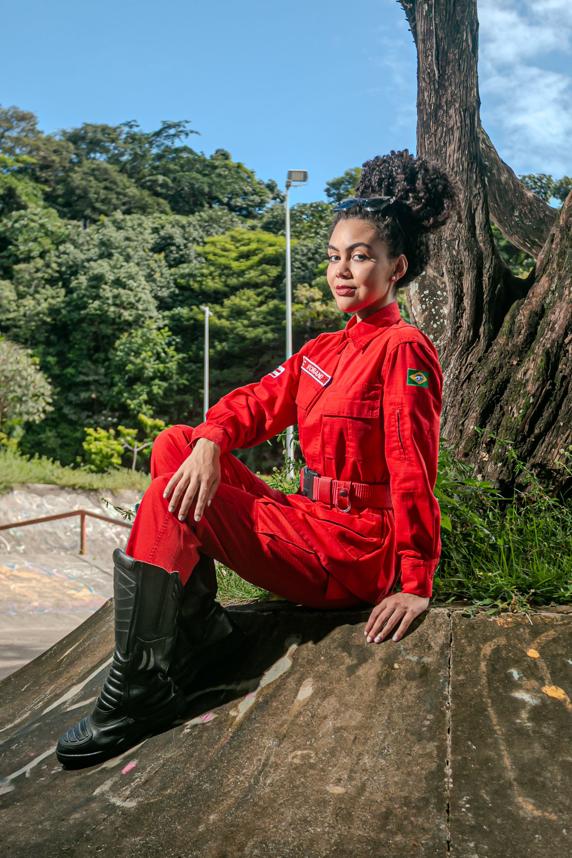 Confident woman in red uniform poses outdoors at a park in Bahia, Brazil.