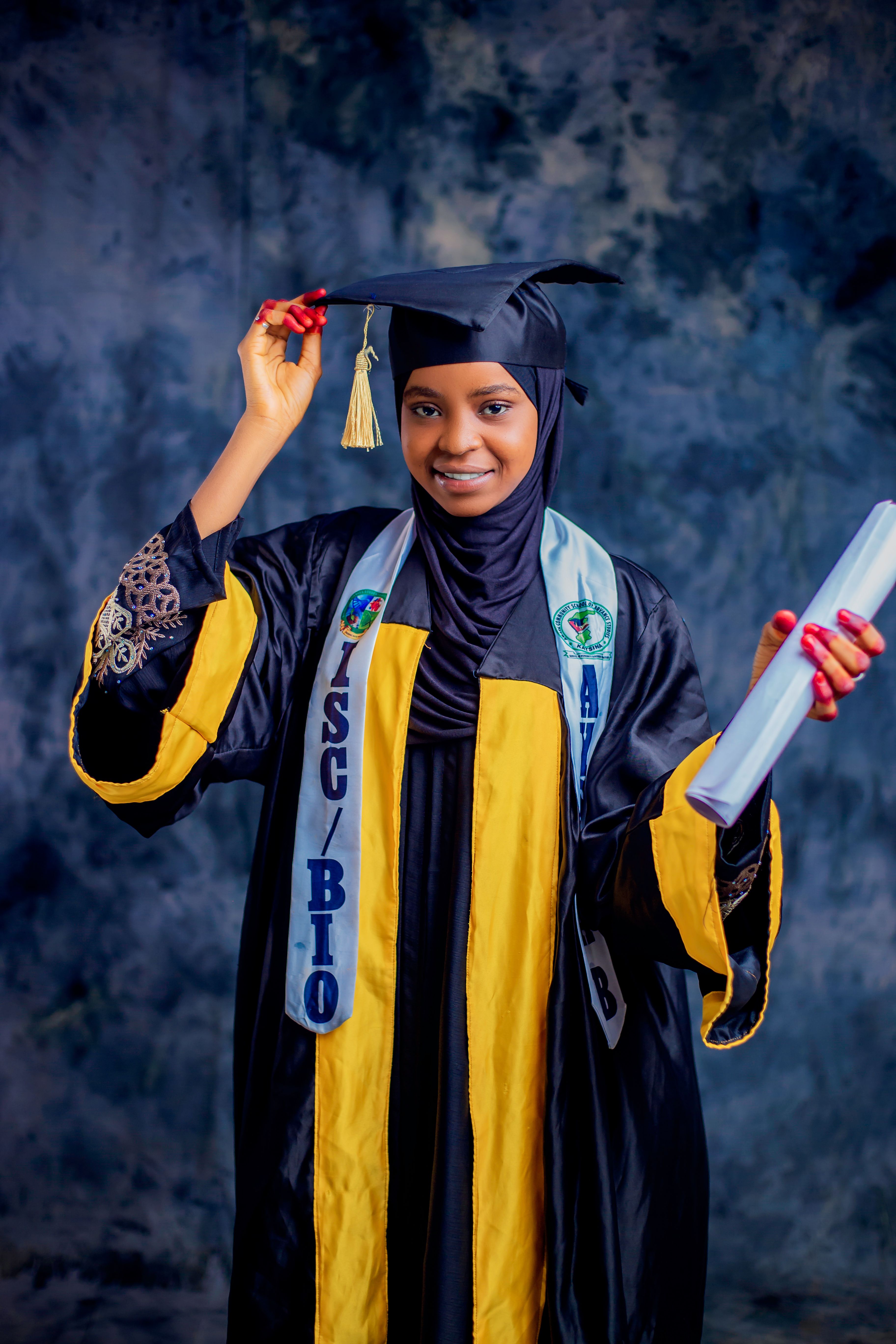 Smiling female graduate in cap and gown holding diploma in studio setting.