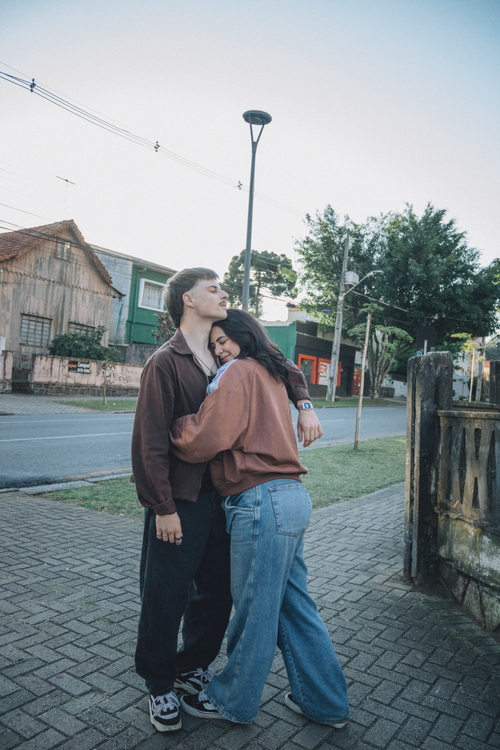 Free A young couple shares a tender embrace on a street corner with trees and houses in the background. Stock Photo