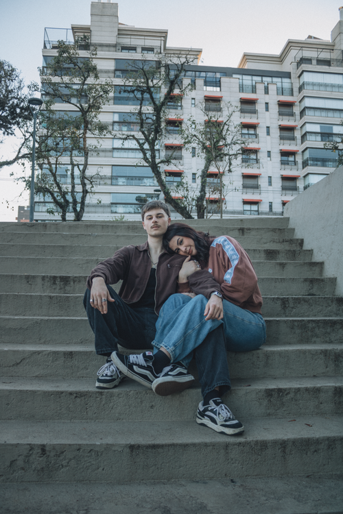 Free Casual young couple sitting on outdoor steps against urban building backdrop. Stock Photo