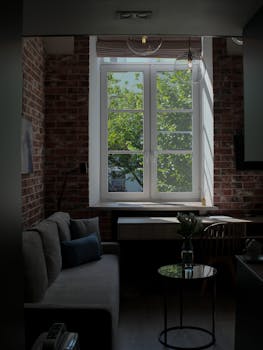 Sunlit room with brick walls, sofa, and desk by large window, showcasing a peaceful setting.
