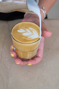 Close-up of a barista creating latte art in a glass cup at a café.