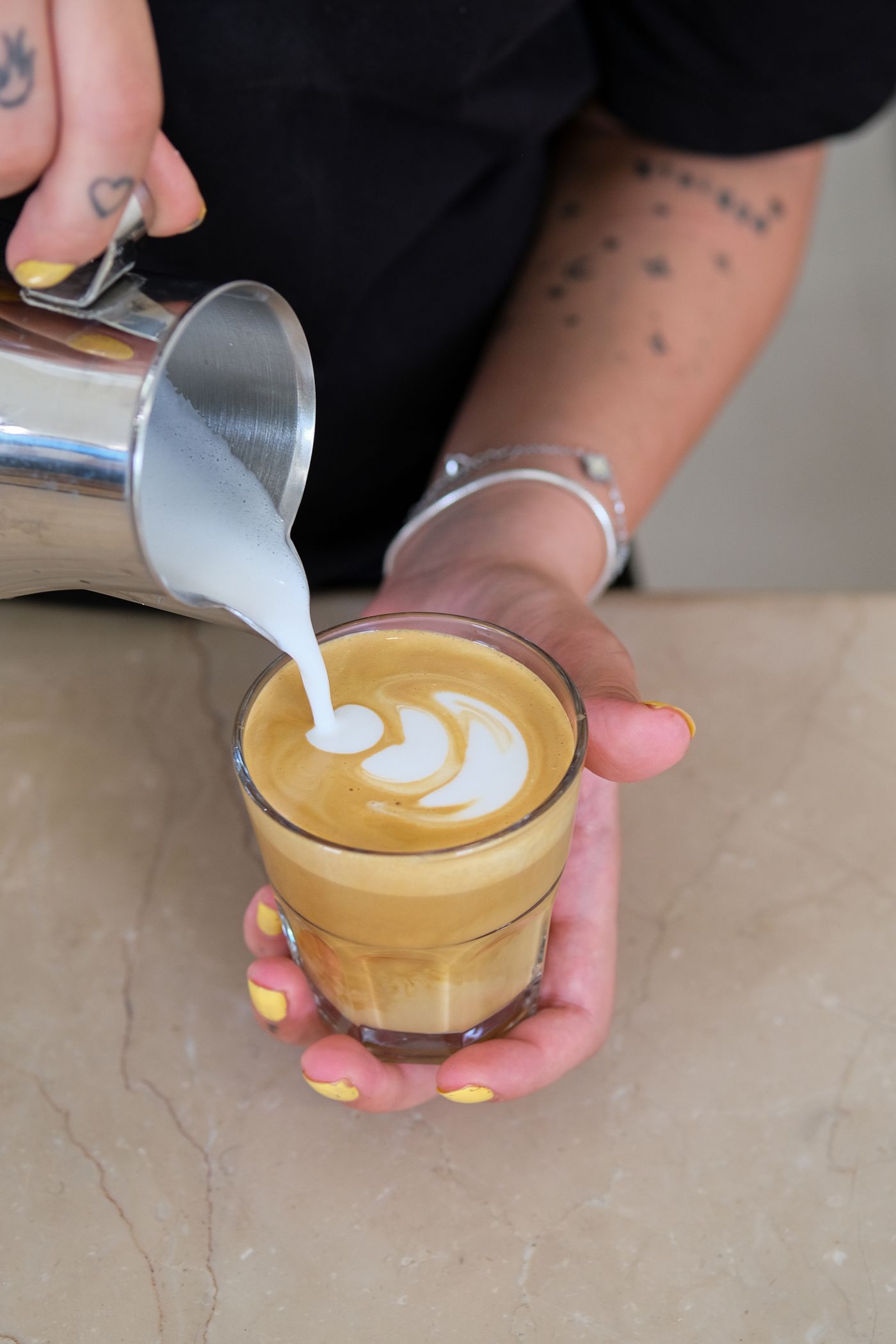 Unbranded stainless-steel milk pitcher creating latte art in a glass