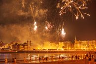 Crowds enjoy vibrant fireworks over the coastal city at night, creating a festive atmosphere.