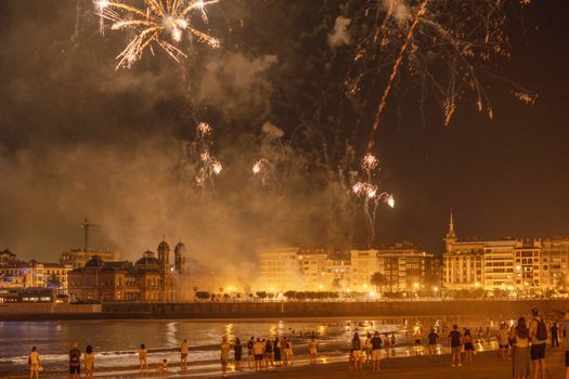 A vibrant night scene with fireworks illuminating the skyline over San Sebastián beach.