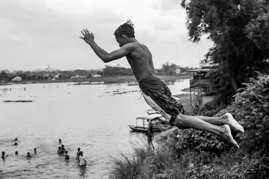 A dynamic black and white photo of a young man jumping into the river in Dhaka, Bangladesh.