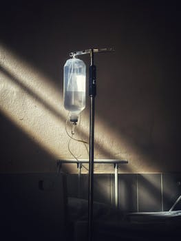 An intravenous drip stand in a quiet hospital room with soft lighting, representing healthcare and solitude.