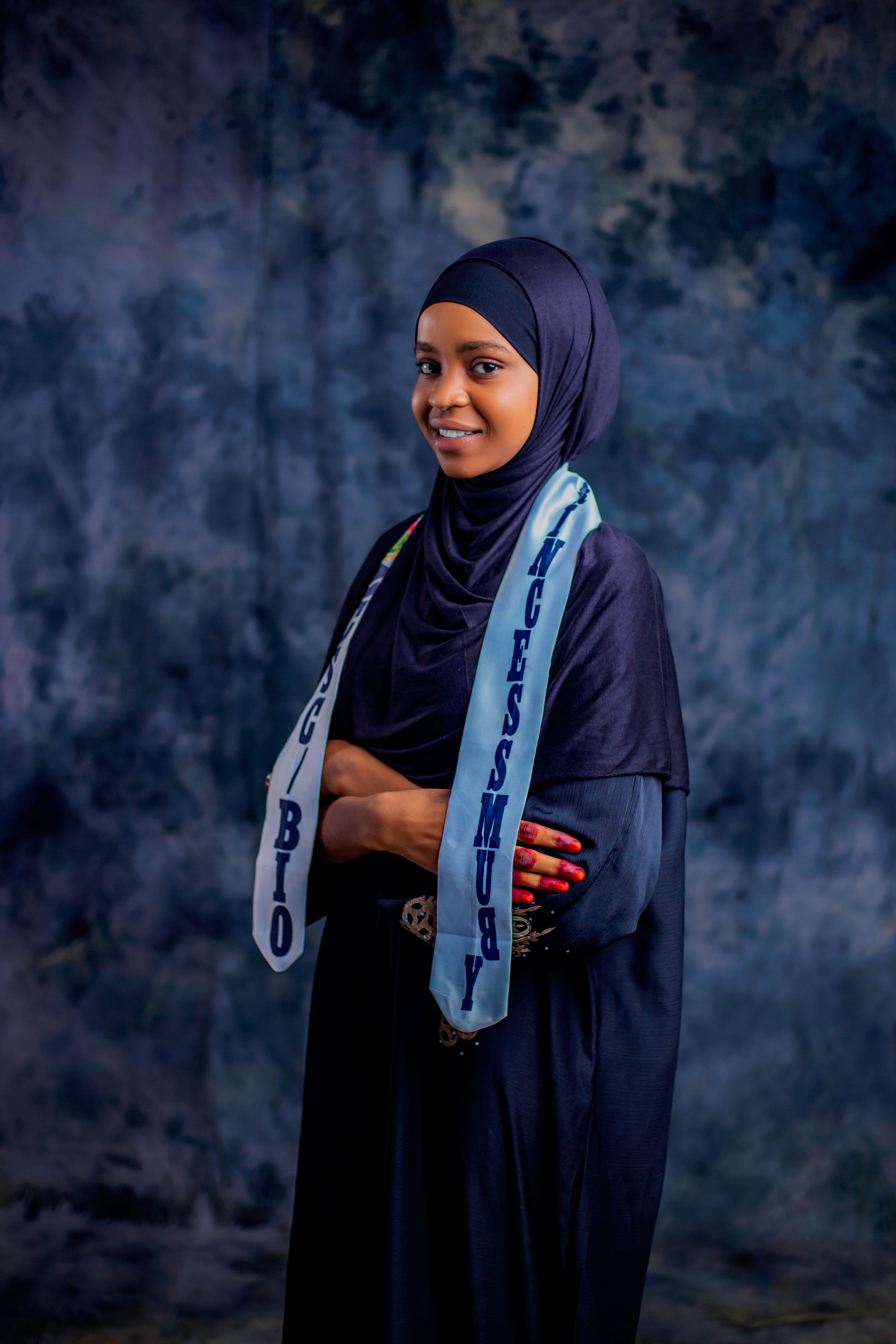 Confident woman in hijab with scarf featuring text, blue textured background.