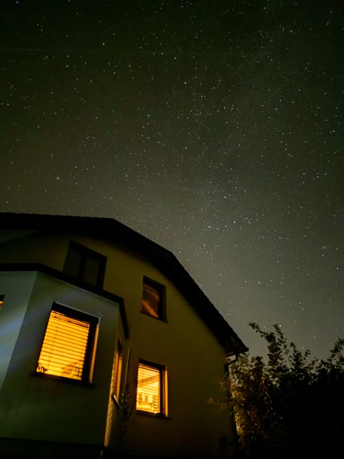 Free A star-filled night sky over a warmly lit house creating a serene nighttime scene. Stock Photo