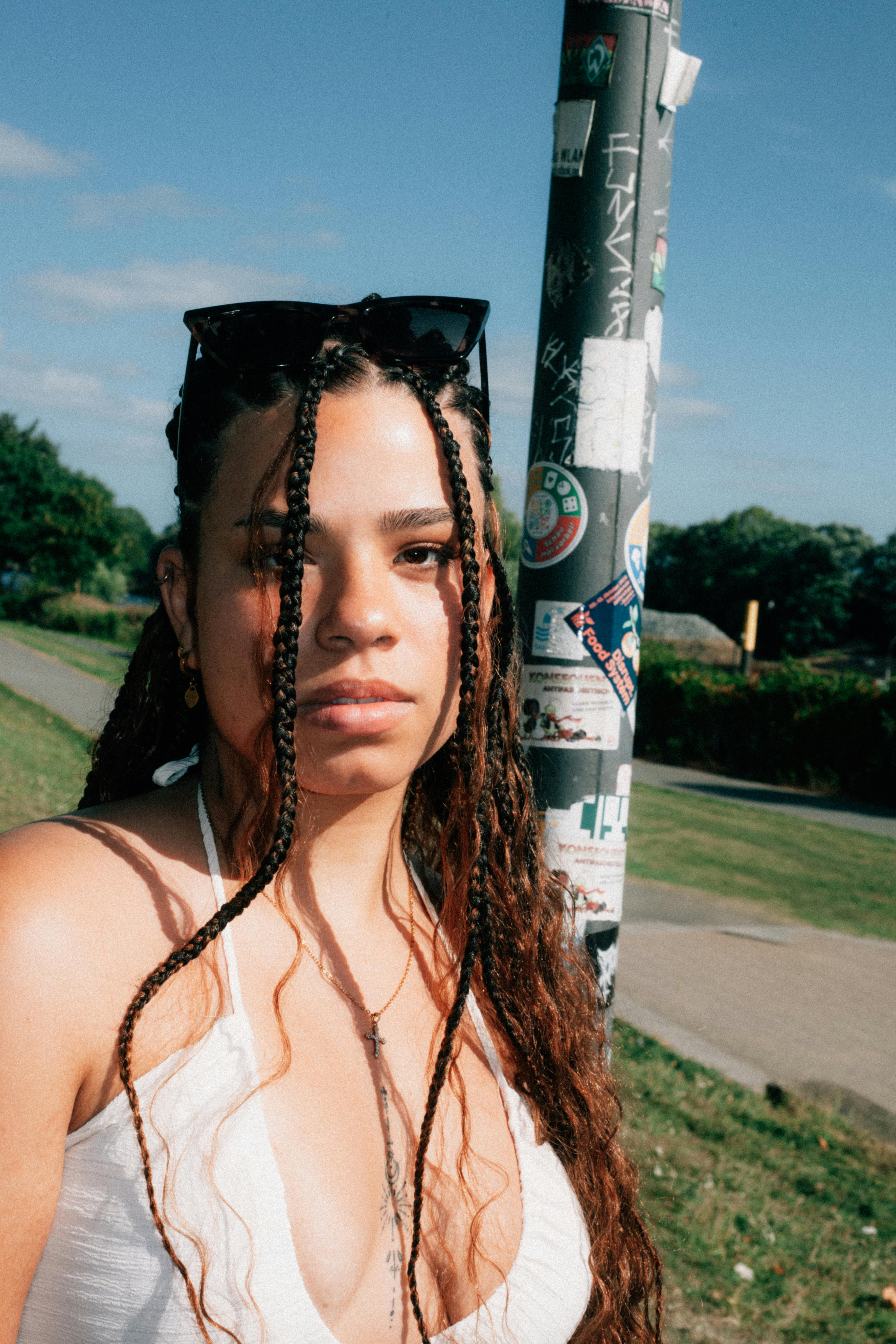 A young woman with braided hair and sunglasses enjoying a sunny day outdoors, showcasing summer vibes.